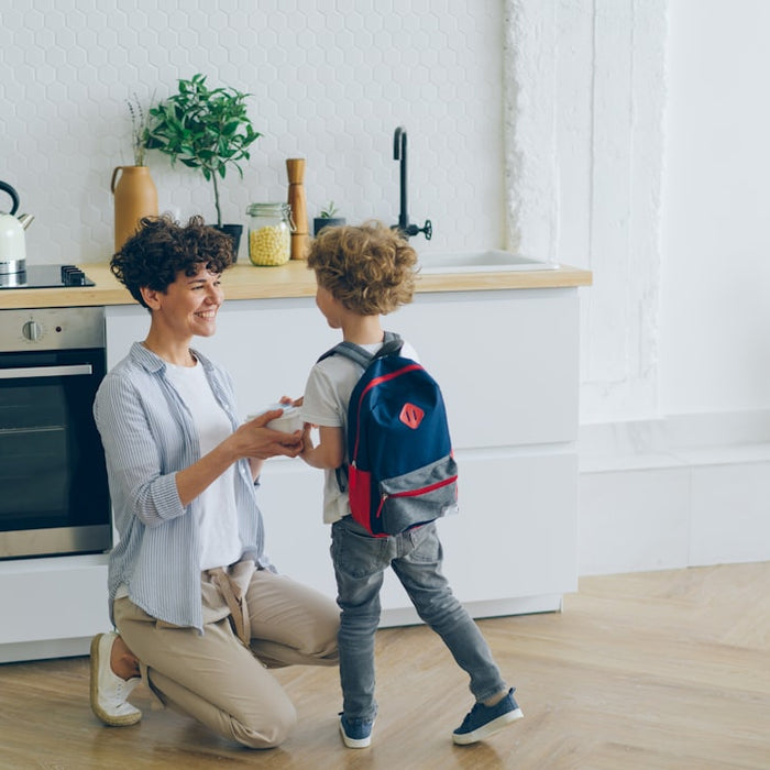 Madre entregando la lonchera a su hijo con la mochila escolar lista en la cocina