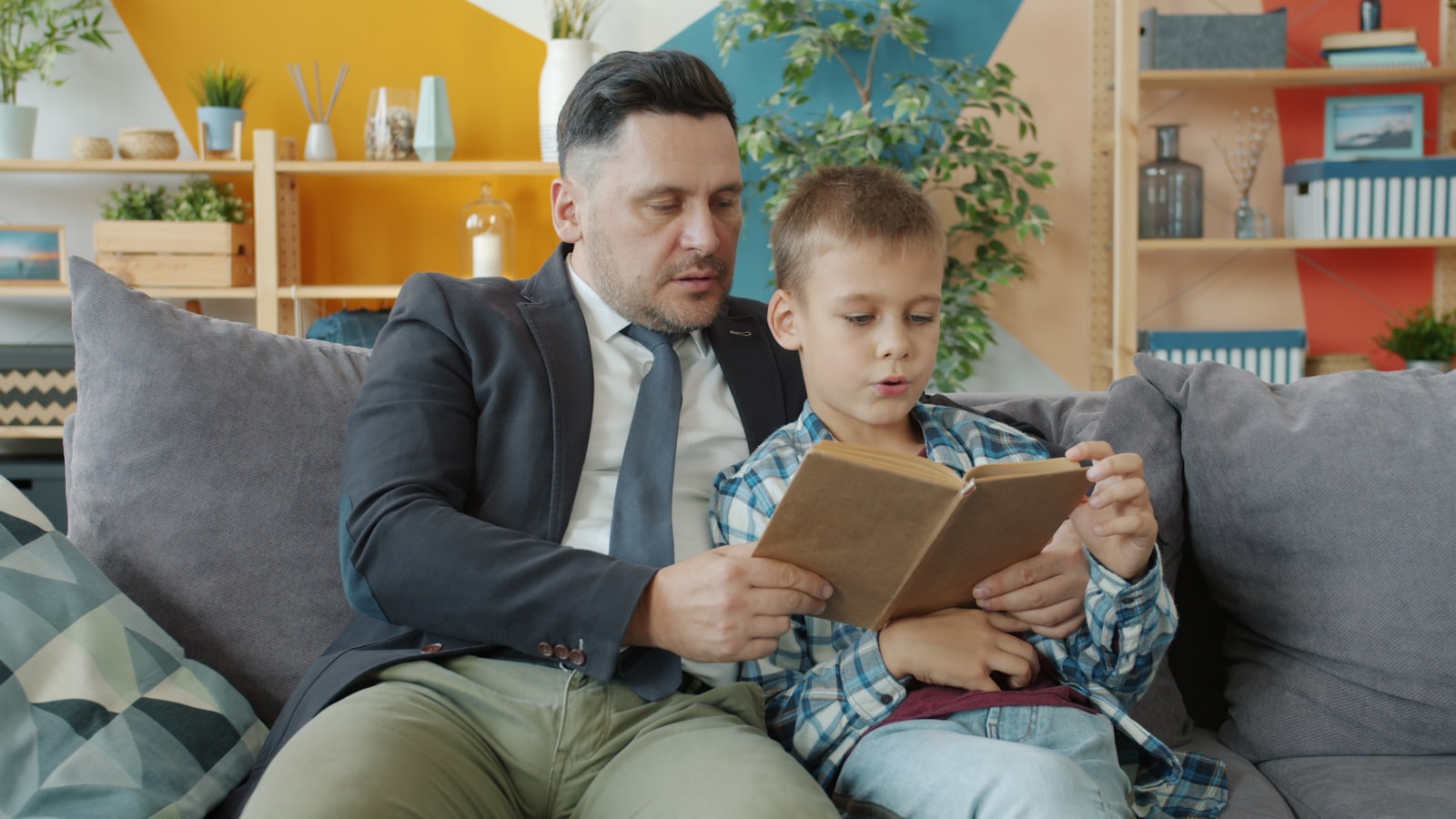 Padre leyendo un libro junto a su hijo en el sofá de casa