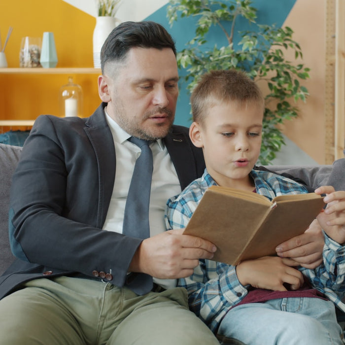 Padre leyendo un libro junto a su hijo en el sofá de casa